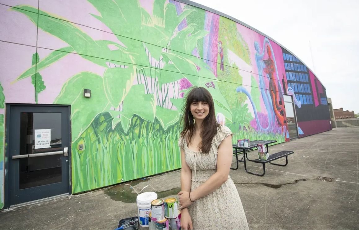 Student stands in front of mural painted on a building